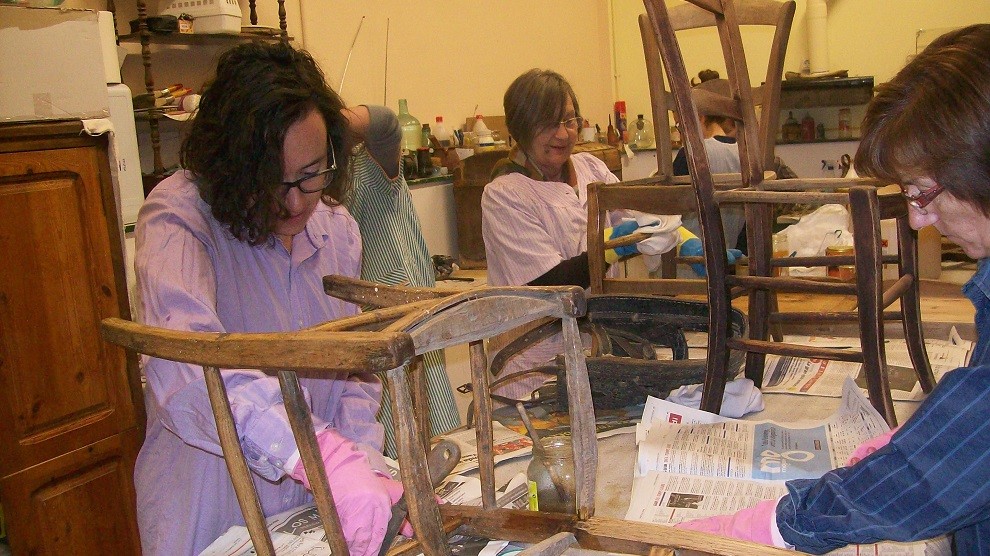 Tres dones reparant unes cadires antigues en un curs de restauració