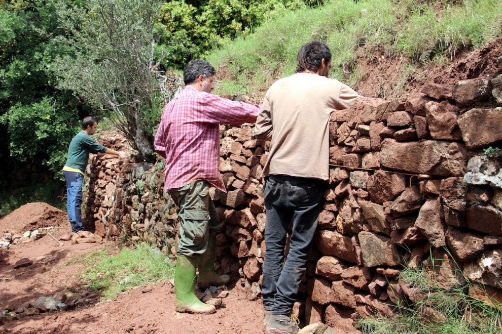 Persones reparant un tros de paret de pedra seca a la ruta del Cinquè Llac